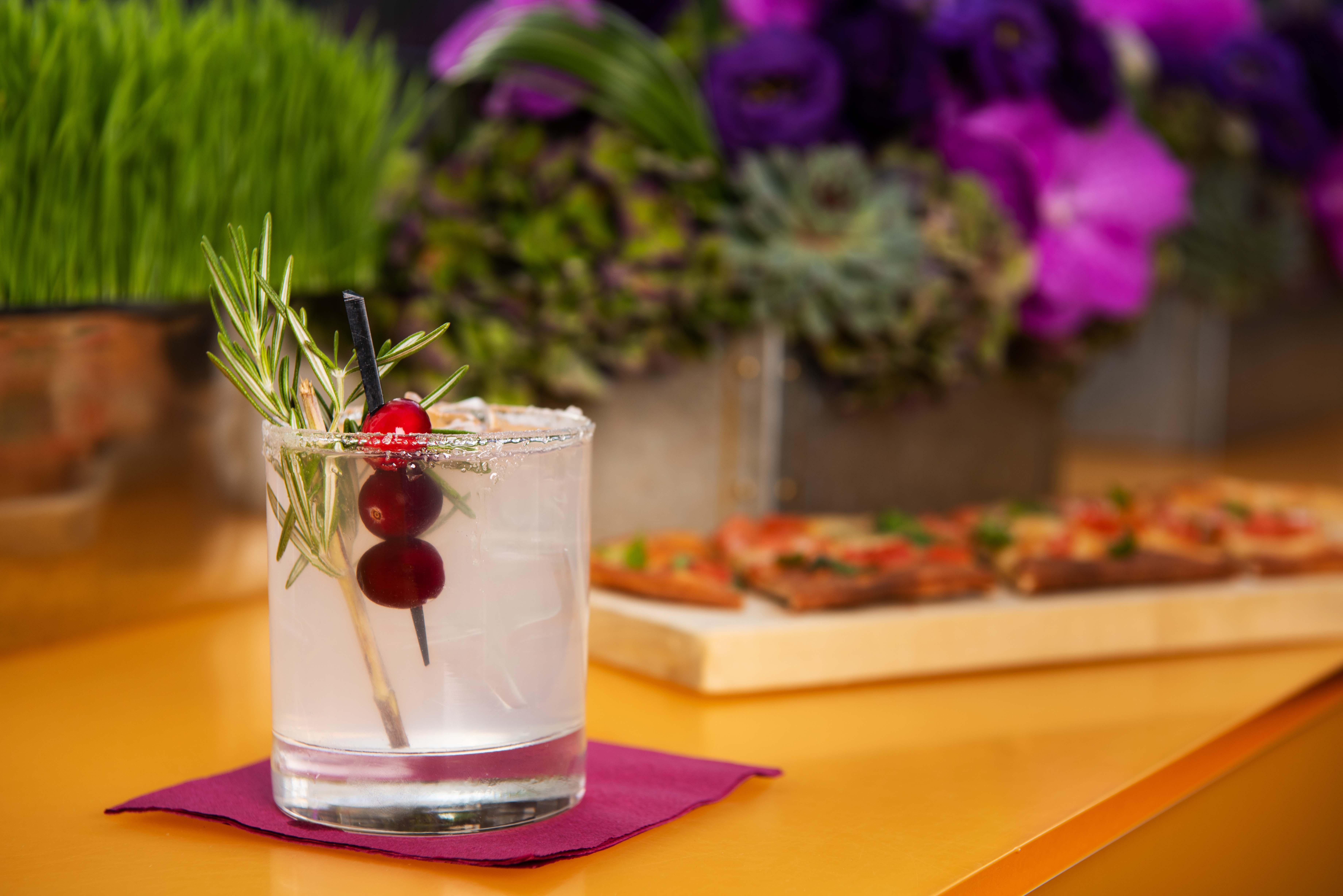 Cocktail with fruit garnish on counter with flatbread pizza